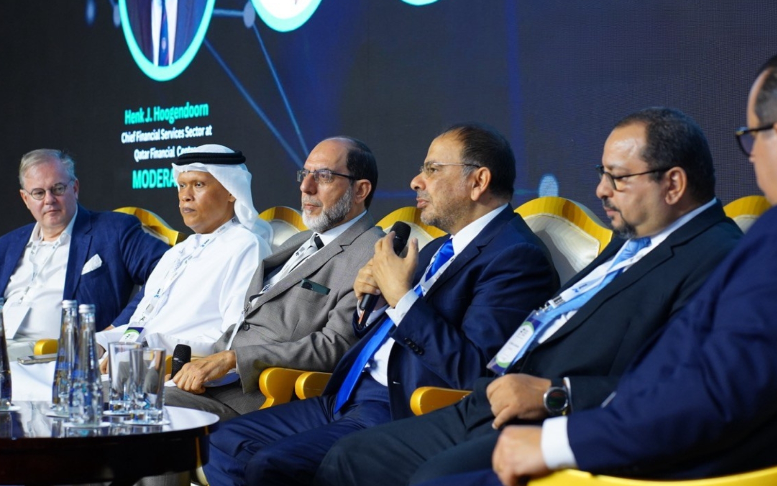 Panellists seated on stage during a forum session, one speaking into a microphone