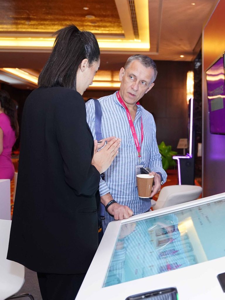 Two delegates in conversation over an interactive display at a technology forum